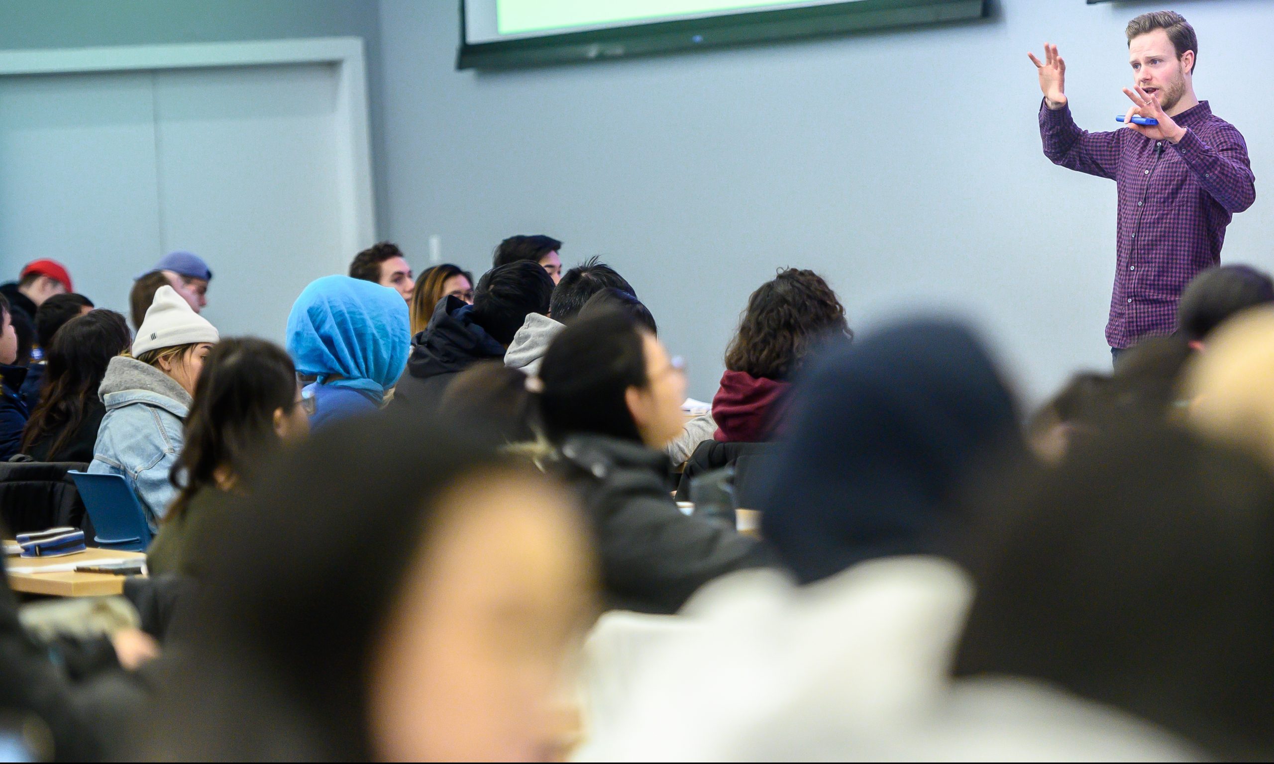 The cover image of the project depicts a UBC professor standing at the front of a room teaching students.