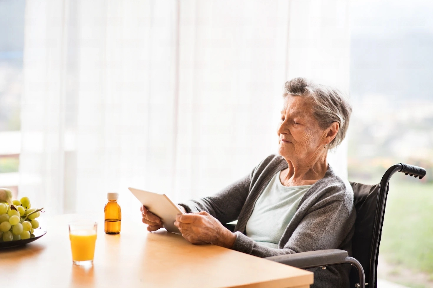 A senior woman sitting in a wheelchair looking at a tablet.
